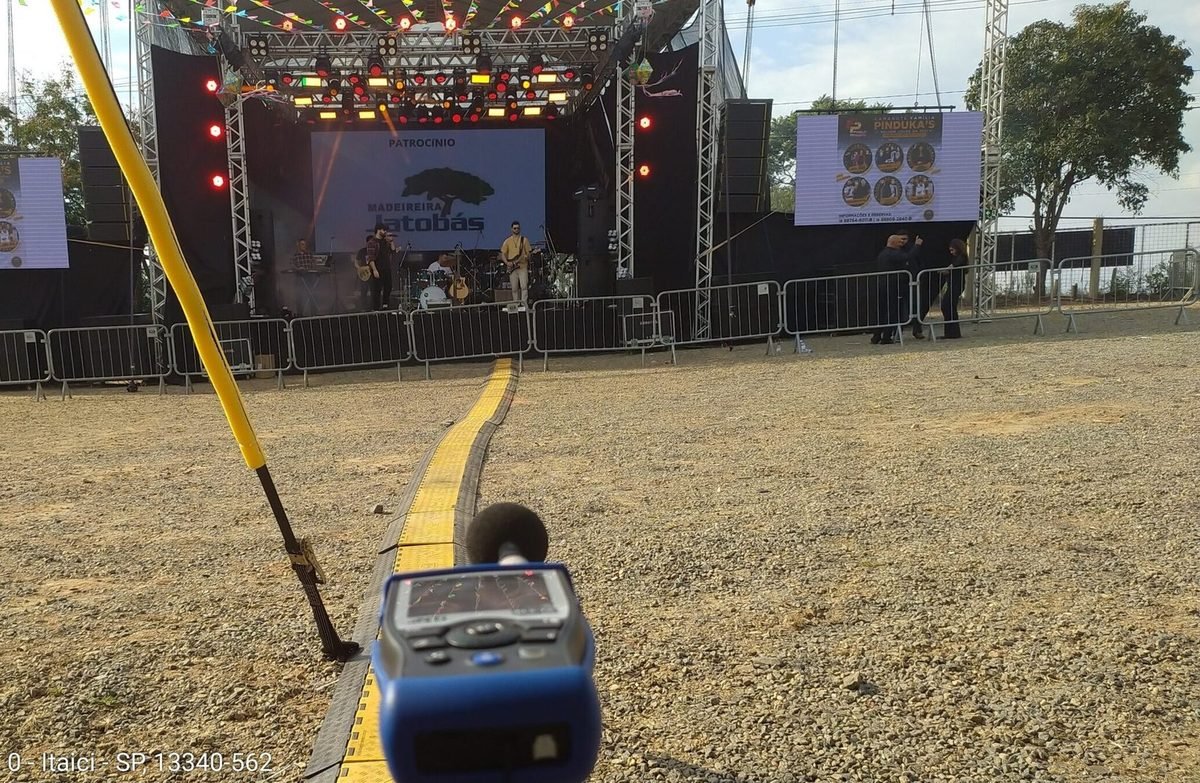 Medição acústica em show com palco e público, microfone de medição em primeiro plano